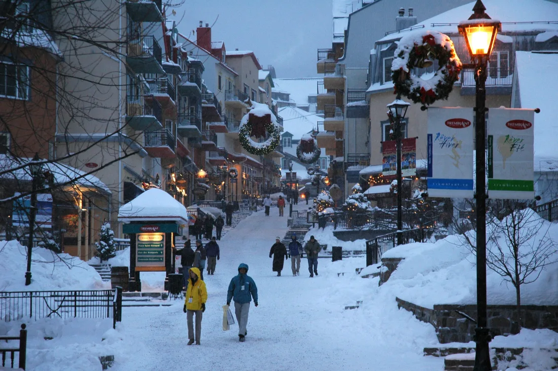Des visiteurs dans le Village piétonnier enneigé de Mont-Tremblant au crépuscule